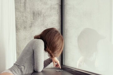 Beautiful сaucasian young woman standing near big panoramic window and looking at mobile phone.