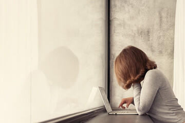 Beautiful сaucasian young woman standing near big panoramic window and looking at laptop.
