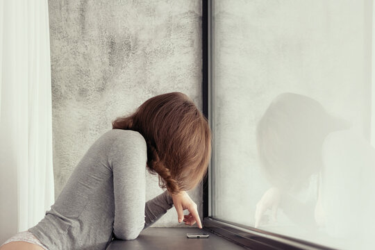 Beautiful сaucasian young woman standing near big panoramic window and looking at mobile phone.