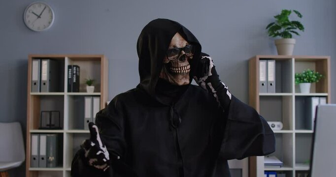 Mobile phone crime, Grim Reaper of Death finding victim online, Internet scam cybercrime fraud, illegal criminal activity, spam, Halloween costume, black hooded cape, skull face mask, skeleton gloves