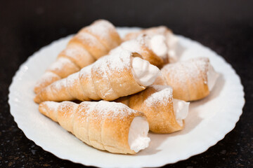 Fragrant puff pastry tubes with whipped cream on a white plate. Cooking sweet pastries, close-up
