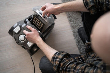Man removing dust container from vacuum cleaner after home cleaning