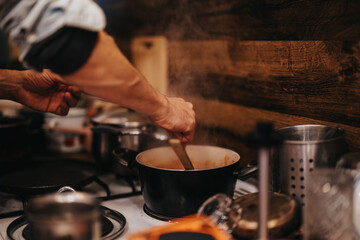 A person cooks on a stove with steaming pots in a warm, rustic kitchen setting. The atmosphere reflects a relaxed and homely vibe, highlighting the enjoyment of preparing homemade food.