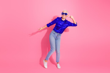Elegant senior woman in vibrant outfit posing stylishly on pink background, showcasing fashion, confidence, and cheerful gestures