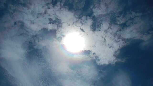 Blue sky, sun, moving white clouds Cirrocumulus and Cirrostratus with colorful Cloud iridescence, Irisation with pearl colors. Topics: sunny, beauty of nature, sun energy, optical phenomenon, weather
