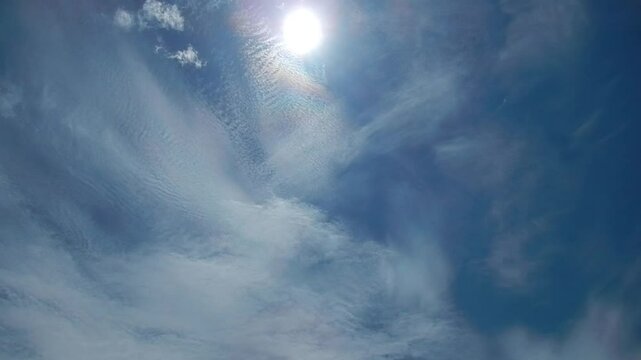 Blue sky, sun, moving white clouds Cirrocumulus and Cirrostratus with colorful Cloud iridescence, Irisation with pearl colors. Topics: beauty of nature, sun energy, optical phenomenon, weather
