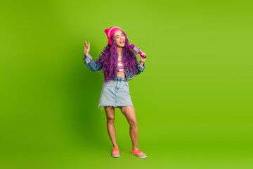 Stylish young woman with purple hair and trendy outfit singing happily with a vibrant green background