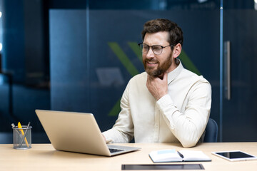 Sick young male office worker sitting at desk with laptop, holding his throat, feeling severe pain