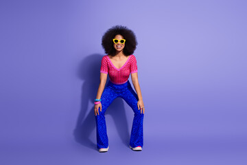 Happy and cheerful young woman with curly hair in retro outfit, smiling against a vibrant purple...