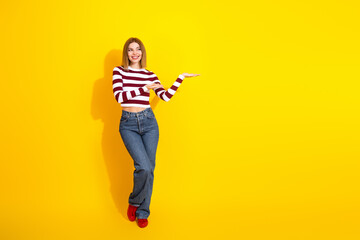 Relaxed young woman in casual striped pullover against vibrant yellow background, posing with happy gesture