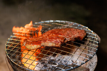 A thick, juicy steak sizzles on a hot grill as flames rise beneath it — capturing the intense heat and flavor of open-fire cooking