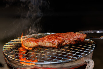 A thick, juicy steak sizzles on a hot grill as flames rise beneath it — capturing the intense...