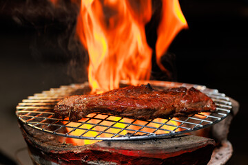 A thick, juicy steak sizzles on a hot grill as flames rise beneath it — capturing the intense heat and flavor of open-fire cooking