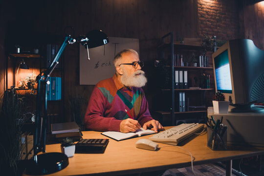 Elderly man working on computer in cozy home office, involved in programming and reflecting on IT and technology advancements
