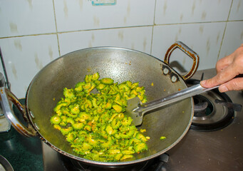 Woman’s Hand Cooking Dry Karela Sabzi in Kadhai, Indian Home Kitchen Scene. Perfect for themes around Indian cuisine, homestyle food, and cultural kitchen moments.