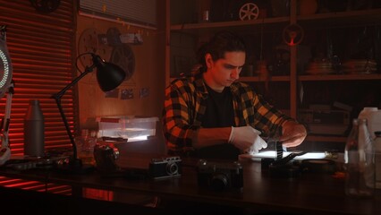 Man Developing Film Negatives in Darkroom with Vintage Cameras