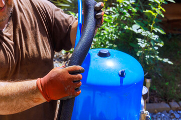 Contractor in gloves is fixing artesian water well pump at home, inspecting black hose