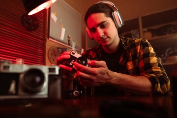Young Man with Headphones Examining Camera in Retro Photography Studio