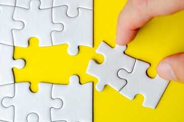 Fototapeta premium Top view of hand taking out of connecting white jigsaw puzzles into its original position on yellow cover background