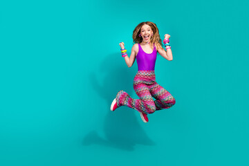 Energetic young woman jumping enthusiastically in colorful retro attire against a vivid teal...