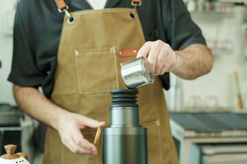 Closeup adult male barista pouring coffee into thermos at cafe, demonstrating artisan dedication, care, and precision, reflecting warmth of small family coffee business, Concept small business
