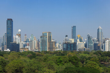 Obraz premium The skyline of Bangkok showcases a blend of contemporary architecture and lush greenery. Skyscrapers rise above the treetops in this vibrant urban setting on a clear day.