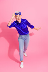 Stylish senior woman in vibrant outfit posing confidently against a colorful pink background,...