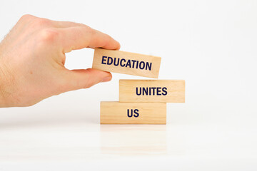 A hand holds wooden blocks displaying the words education, unites, and us. The blocks are arranged in a way that emphasizes the importance of collaboration in learning