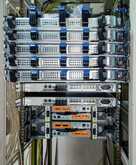Rear view of servers, switches and storage devices in a rack mounted one above the other. Power and optical cables are visible