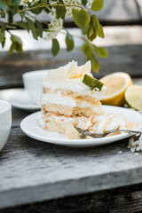 A broken slice of lemon-lime sponge cake with white chocolate drizzle, elegantly placed on a vintage ceramic plate with linen napkins and scattered chamomile flowers, creating a cozy cottagecore