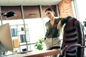 Young professional businesswoman standing thoughtfully in a modern office with a confident and...