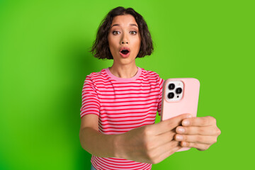Young woman with surprised expression holding a smartphone, wearing a striped t-shirt against a...