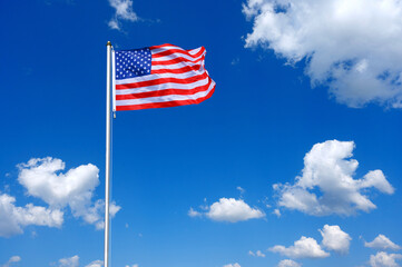 The flag of United States  flutters in the wind in a blue sky with white clouds