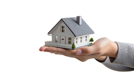 A hand holding a miniature house with a gray roof and white picket fence on a black background scene on transparent background