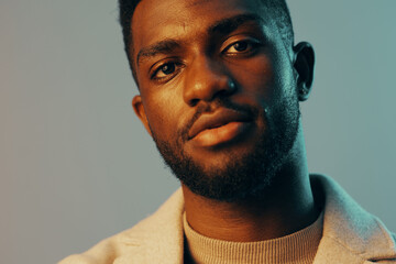 Obraz premium Confident young African man in stylish attire with soft lighting, showcasing a cool expression against a minimalist blue backdrop