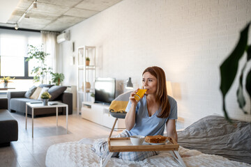 Woman enjoying breakfast in bed with orange juice and waffles