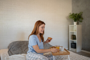 Happy woman enjoying breakfast in bed in pajamas