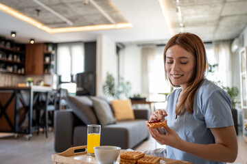 Woman spreading jam on waffles for breakfast in modern apartment