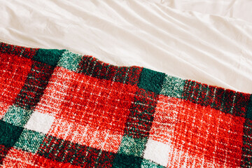 Cozy red and green plaid blanket draped over soft white bedding in a warm indoor setting