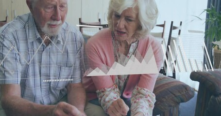 senior couple leaning forward studying finances in home lounge, with animated bar charts overlay - Powered by Adobe