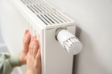 Close-up of small child&rsquo;s hands warming on white home radiator. Winter heating, indoor comfort, safe temperature control, family energy use, cozy atmosphere and home warmth concept.