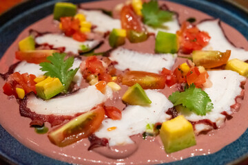 Octopus Al Olivo served on plate. It is sliced octopus sashimi with greek kalamata olive mayonnaise, olive oil, avocado, corn and tomato chalaca sauce.