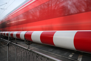 Bahnschranke rot-weiß und vorbeifahrender roter Zug - Stockfoto