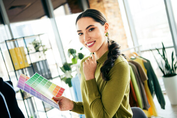 Young professional entrepreneur holding color palettes in a stylish atelier with racks of clothes...