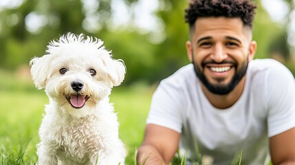 Smiling man lying next to a white dog is showing affection in a grassy outdoor environment.