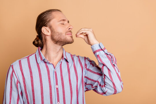 Confident young man with bearded face in casual striped shirt gesturing passionately against beige background showcasing modern elegance