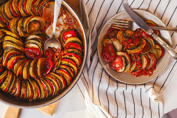 Homemade ratatouille preparation and serving. Child's hands placing vegetable slices into a baking...