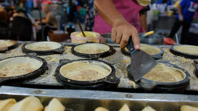 Street vendor preparing apam balik, a popular malaysian street food pancake with peanuts and sugar.