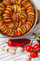Homemade ratatouille preparation and serving. Child's hands placing vegetable slices into a baking...