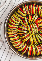 Homemade ratatouille preparation and serving. Child's hands placing vegetable slices into a baking...